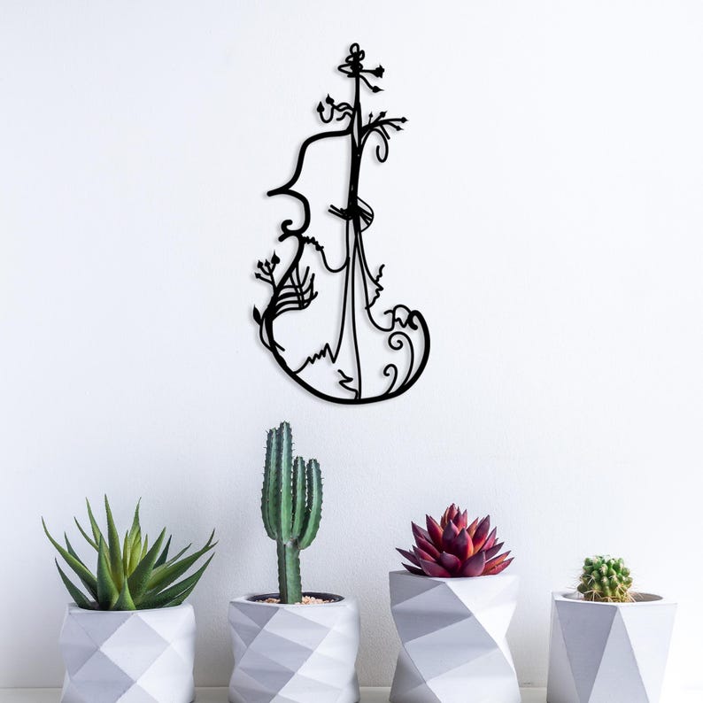 May include: Black metal wall art sculpture of a stylised violin with floral details. The sculpture is mounted on a white wall and there are three potted plants in the foreground.