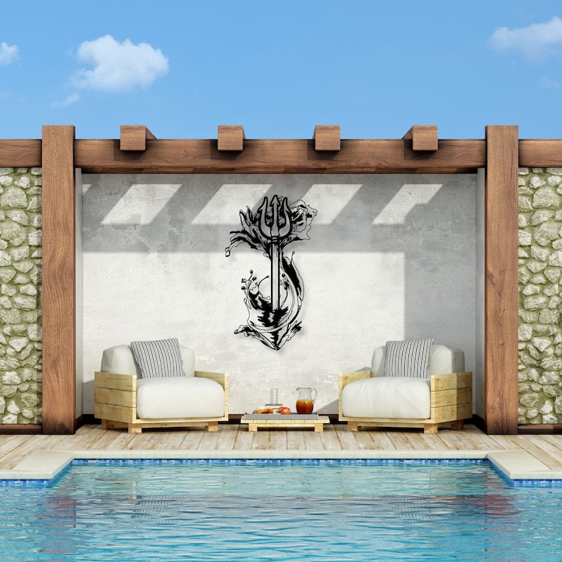 May include: Black metal wall art depicting a trident with waves crashing around it. The art is mounted on a white wall in a backyard setting with a swimming pool and lounge chairs.