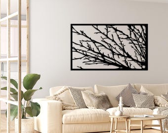 May include: Black metal wall art featuring a silhouette of bare tree branches against a white background. The art is displayed on a white wall above a white couch with pillows.