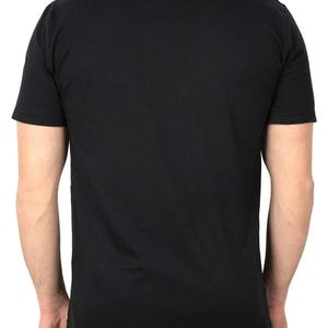 May include: A black crew neck t-shirt with short sleeves. The back of the shirt is visible, showing the shoulders and upper back. The shirt is made of a soft, opaque material.
