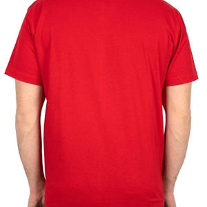 May include: A solid red crew neck t-shirt. The short-sleeved shirt is made of a soft material. The back of the shirt is visible, showing the shoulders and upper arms. The shirt is a vibrant, bright red color.