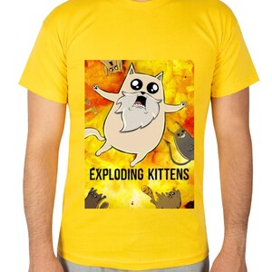 May include: Yellow t-shirt featuring a cartoon image of a cat with a long white beard and the text "EXPLODING KITTENS". The cat is surrounded by other cartoon cats on a yellow and orange background.