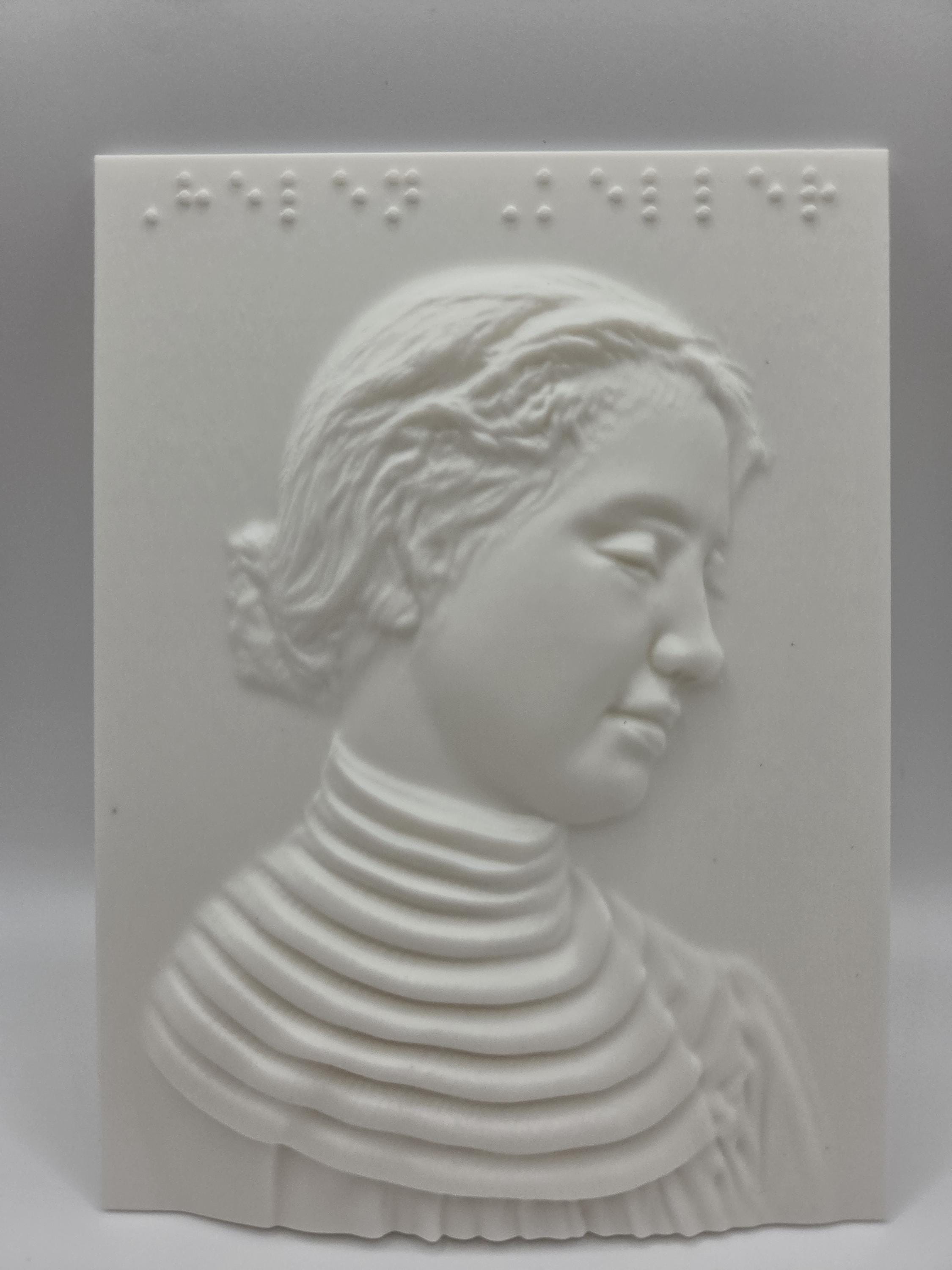 White tactile relief portrait of Helen Keller in profile, hair pinned back and wearing a high ruffled collar, with Braille across the top reading Helen Keller.
