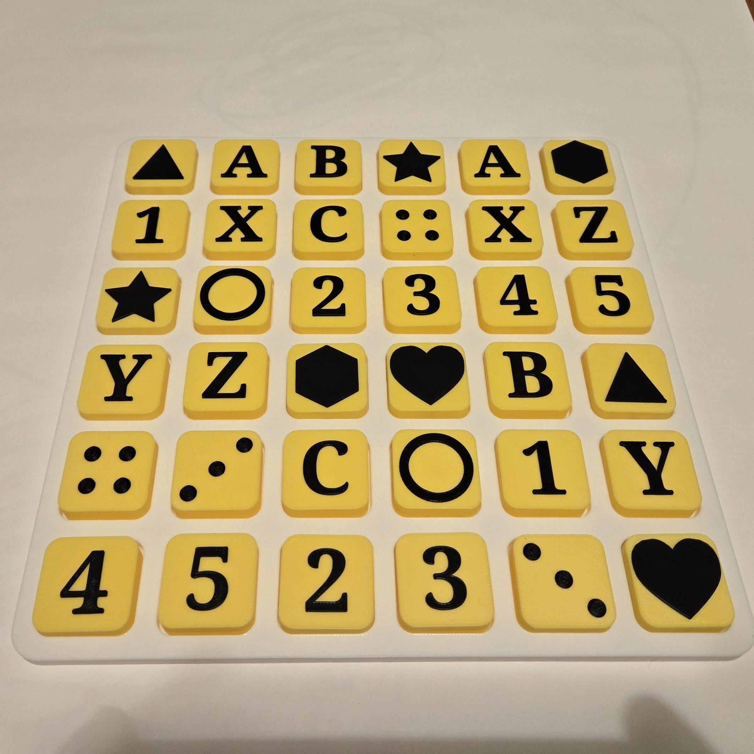 Six-by-six grid of yellow tiles on a white tray, all face up, showing raised black letters, numbers, Braille dot patterns and shapes such as stars, hearts, circles, hexagons and triangles.