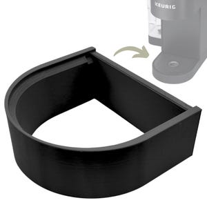 May include: Black plastic coffee pod holder designed to fit under a Keurig coffee maker. The holder is shaped like a half-circle and has a smooth, textured surface.