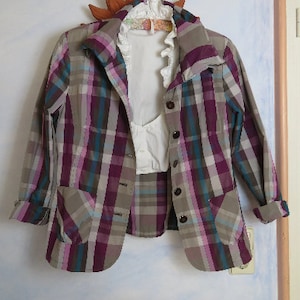 May include: A plaid jacket with a brown, purple, and blue pattern. The jacket has a collar and two pockets. It is hanging on a hanger.