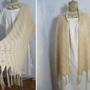 以下が含まれることがあります： フリンジが付いたベージュのクロシェのショール。ショールは白いマネキンにかけられています。