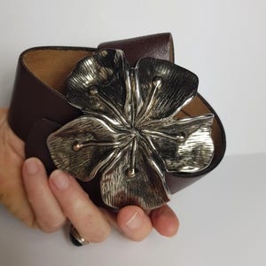 May include: A brown leather belt with a large silver flower buckle.