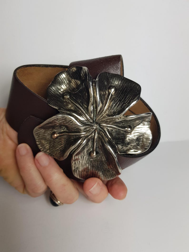 May include: A brown leather belt with a large silver flower buckle.