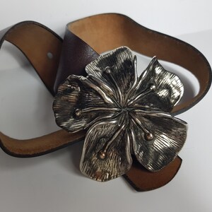 May include: A brown leather belt with a large silver flower buckle.