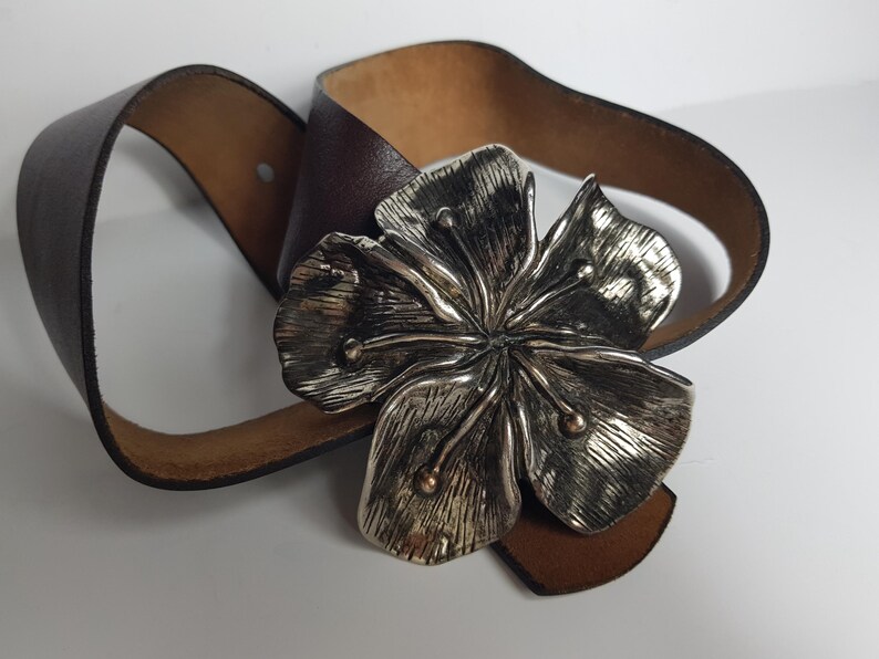 May include: A brown leather belt with a large silver flower buckle.