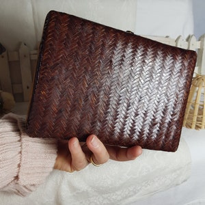 Puede incluir: Un bolso de mano tejido marrón con un diseño tejido blanco. El bolso tiene una forma rectangular y un cierre de broche.