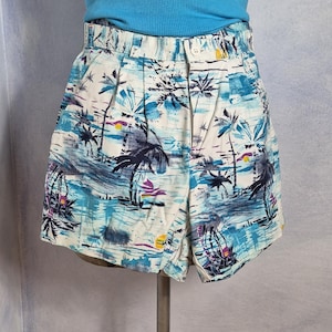 Könnte beinhalten: Hoch taillierte Shorts mit tropischem Druck aus Palmen, blauem Wasser und gelben Sonnenakzenten auf weißem Grund. Die Shorts haben eine gefaltete Vorderseite, einen Knopfverschluss und einen Bund mit Gürtelschlaufen, kombiniert mit einem blauen Ripp-Top.