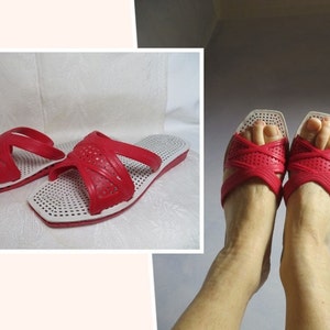Könnte beinhalten: Ein Paar rot-weiße Sandalen mit einem Kreuzriemen-Design. Die Sandalen haben eine weiße Sohle und ein rotes Obermaterial mit einem perforierten Muster.