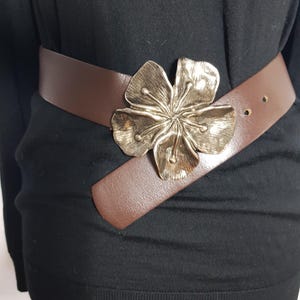 May include: A brown leather belt with a large silver flower buckle.