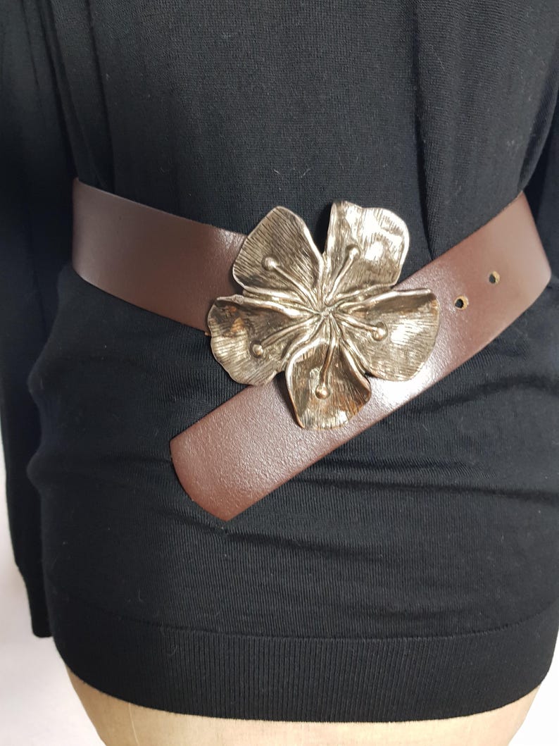 May include: A brown leather belt with a large silver flower buckle.