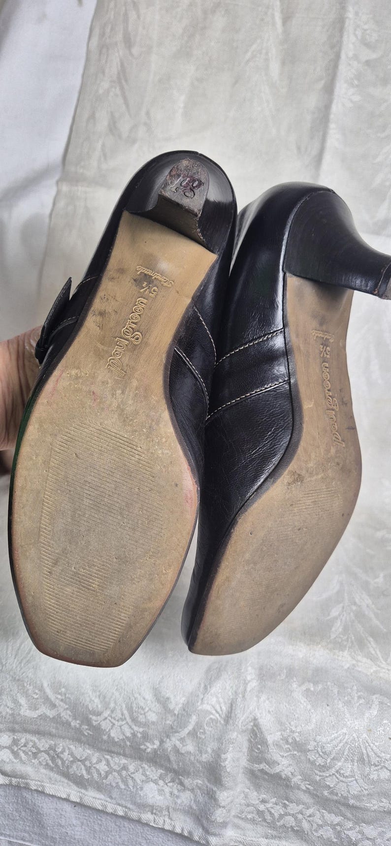 May include: Pair of black leather heeled shoes with a buckle closure. The soles are worn and show the brand name "Paul Green". The heels are approximately 2.5 inches high.