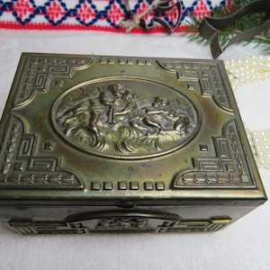 May include: A vintage brass trinket box with an ornate design featuring cherubs and a floral motif. The box has a hinged lid and a decorative base.