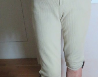 May include: A person wearing a light brown sweater and beige corduroy pants with a tie at the bottom. They are wearing brown shoes with a strap.