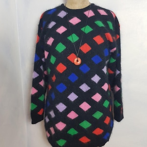 May include: Black fuzzy sweater with a colorful diamond pattern. The sweater has a crew neck and long sleeves. A red pendant hangs from a black cord necklace.