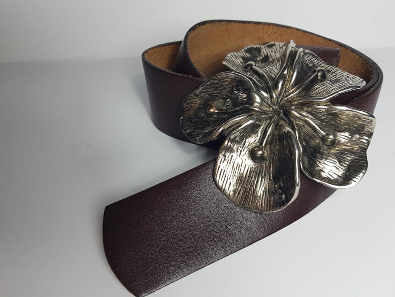 May include: A brown leather belt with a silver flower buckle