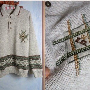 Könnte beinhalten: Ein beiger Strickpullover mit einem grün-braun-weißen Musterband am unteren Ende der Ärmel und am unteren Ende des Pullovers. Der Pullover hat einen Knopfkrag und ein kleines gesticktes Emblem auf der linken Brust mit den Buchstaben "LG" und einer Krone.
