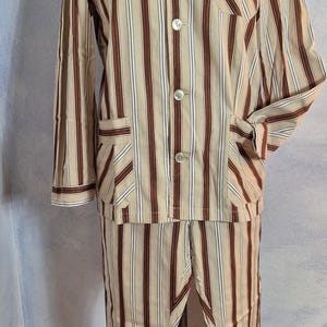 May include: A vintage pajama set with a beige background and vertical stripes in brown and white. The long-sleeved top has a button-down front, a chest pocket, and two front pockets. The matching pants have a relaxed fit.