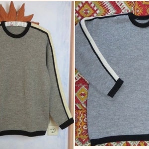 May include: Two grey sweaters with black and white stripes on the sleeves. The sweaters have a black trim around the neck and bottom.