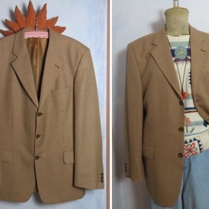 Könnte beinhalten: Ein brauner Blazer mit kariertem Muster und drei Knöpfen. Der Blazer hat einen Schalkragen und Pattentaschen.