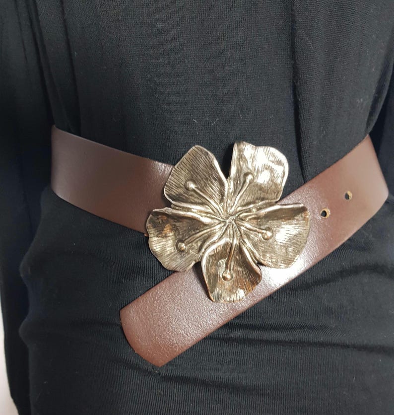 May include: A brown leather belt with a large silver flower buckle.