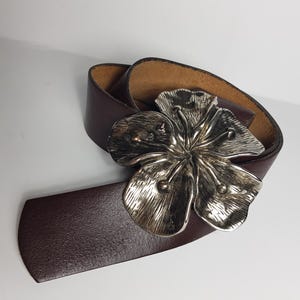 May include: A brown leather belt with a silver flower buckle.