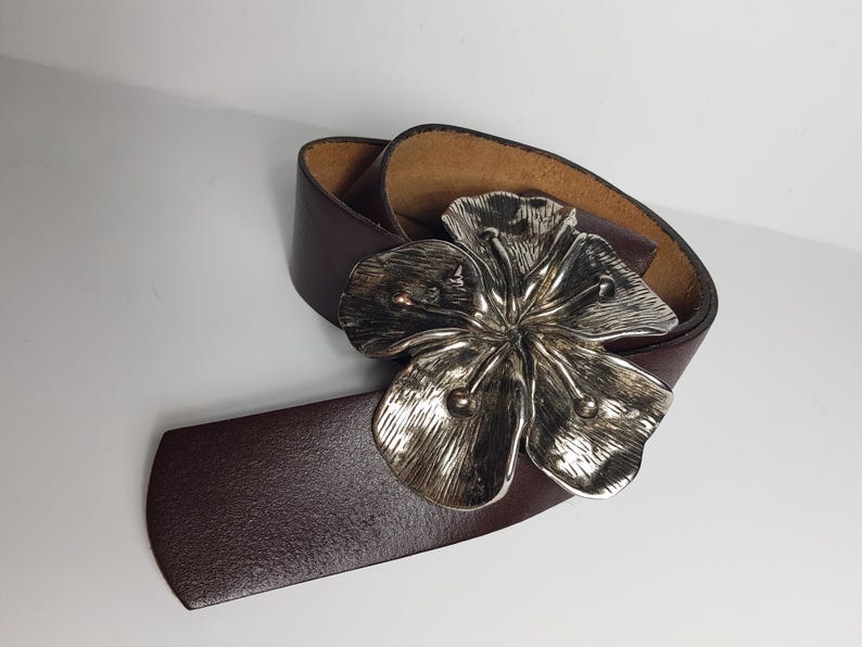 May include: A brown leather belt with a silver flower buckle.