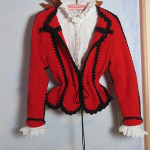 May include: A red crocheted jacket with black trim and a white lace collar. The jacket has a cinched waist and a black drawstring.