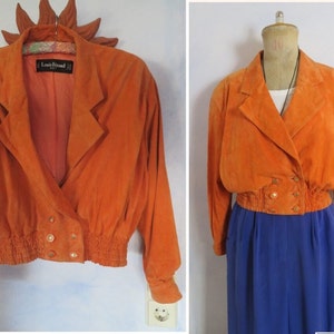 Puede incluir: Una chaqueta de ante naranja recortada con cierre de doble botonadura y cintura ajustada. La chaqueta tiene botones dorados y una etiqueta que dice "Laura Perelli".