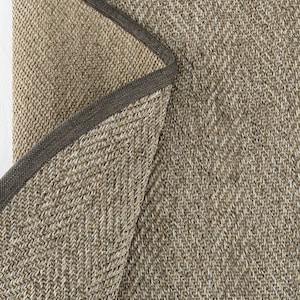 May include: A close-up of a beige and brown woven rug with a dark brown border. The rug has a herringbone pattern.