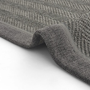 May include: Close-up of a grey rug with a textured, woven design. The rug has a folded corner, revealing the thickness and detail of the material. The colour is a neutral grey, suitable for various interior styles.