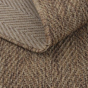 Peut inclure: Un tapis marron présentant un motif à chevrons tissé dense avec une texture visible. Le tapis est replié au coin supérieur, révélant le dessous du tissage et un bord fini et cousu qui correspond à la couleur du tapis.
