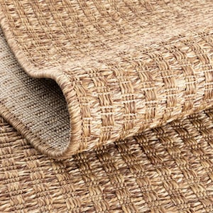 Può includere: Primo piano di un tappeto tessuto con un motivo geometrico strutturato. Il tappeto è una miscela di tonalità marroni chiare e medie, con un bordo arrotolato che rivela un lato inferiore più chiaro. La trama crea un design a griglia.