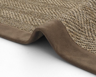 May include: A brown woven rug with a brown suede border. The rug is folded in half, showing the underside of the rug.