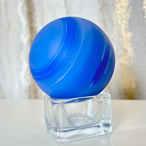 Puede incluir: Un orbe de vidrio azul con remolinos blancos sobre una base cuadrada de vidrio transparente.