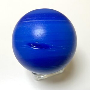 Puede incluir: Un modelo de globo azul y blanco del planeta Neptuno. El globo est&aacute; en un soporte transparente.