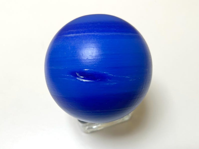 Puede incluir: Un modelo de globo azul y blanco del planeta Neptuno. El globo est&aacute; en un soporte transparente.