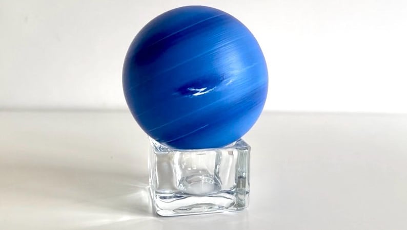 Puede incluir: Una esfera de vidrio azul con vetas blancas, que se asemeja a un planeta, se asienta sobre un soporte de vidrio transparente en forma de cubo.