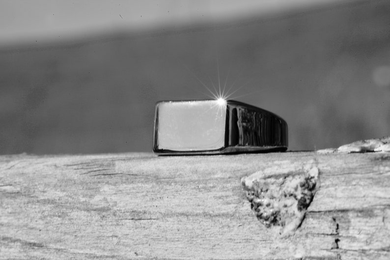 May include: A silver signet ring with a rectangular top. The ring is sitting on a wooden surface.