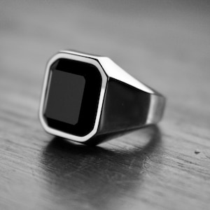 May include: A silver ring with a black square-shaped gemstone.
