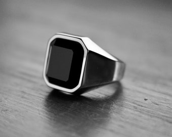 May include: A silver ring with a black square-shaped gemstone.