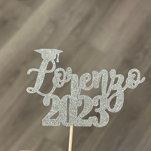 Puede incluir: Topper para pastel de graduación de brillo plateado con el nombre Lorenzo y el año 2023.