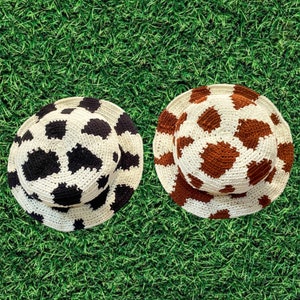 May include: Two crocheted bucket hats with a cow print pattern. One hat is black and white, and the other is brown and white.