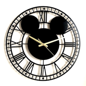 May include: Black metal wall clock with Roman numeral markings and gold-coloured hands. The clock face is shaped like Mickey Mouse's head with two black circles for ears.