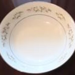May include: A white ceramic serving bowl with a gold rim and a delicate floral pattern in shades of green and pink. The bowl has a wide, shallow design, suitable for serving salads or pasta dishes.